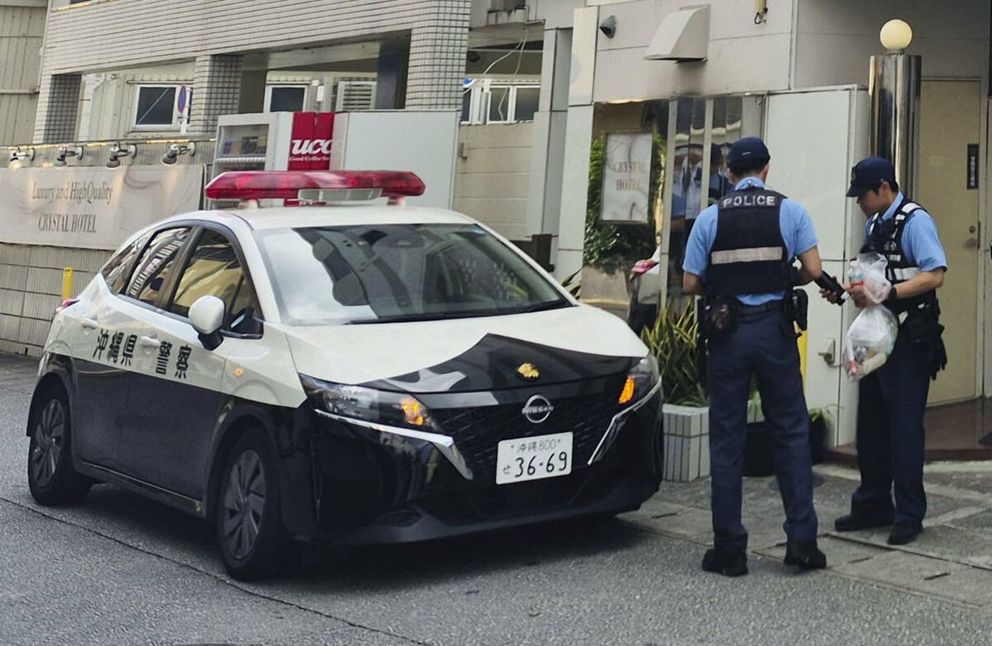 Police officers behind tape near a Naha hotel during an investigation